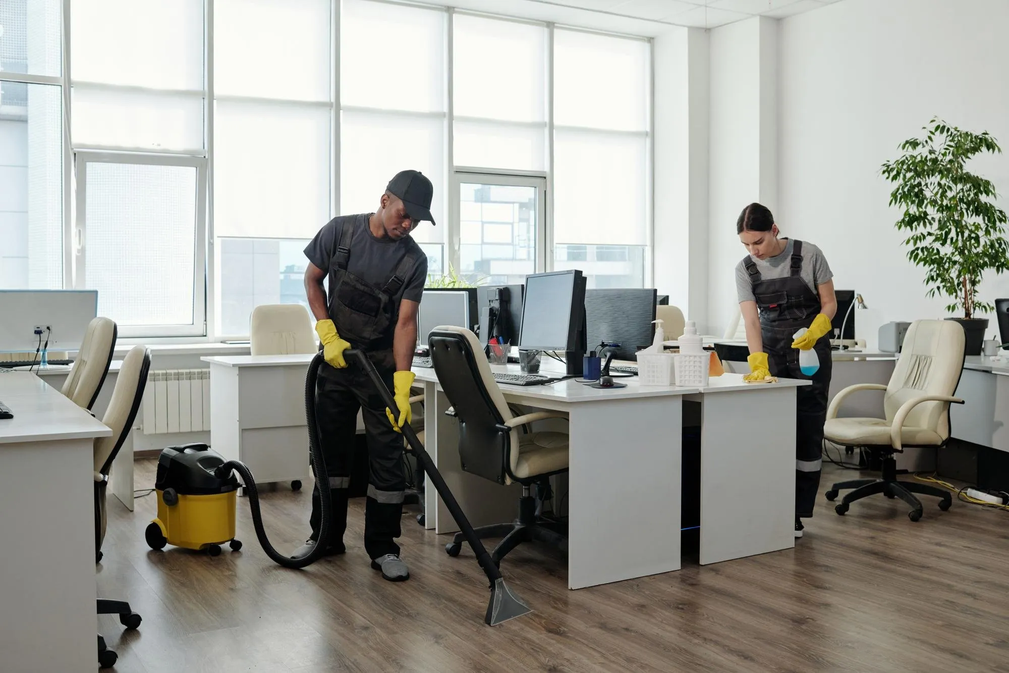Two DITA Pro Clean cleaners in uniform vacuuming and wiping desks in a bright Metro Detroit open-plan office